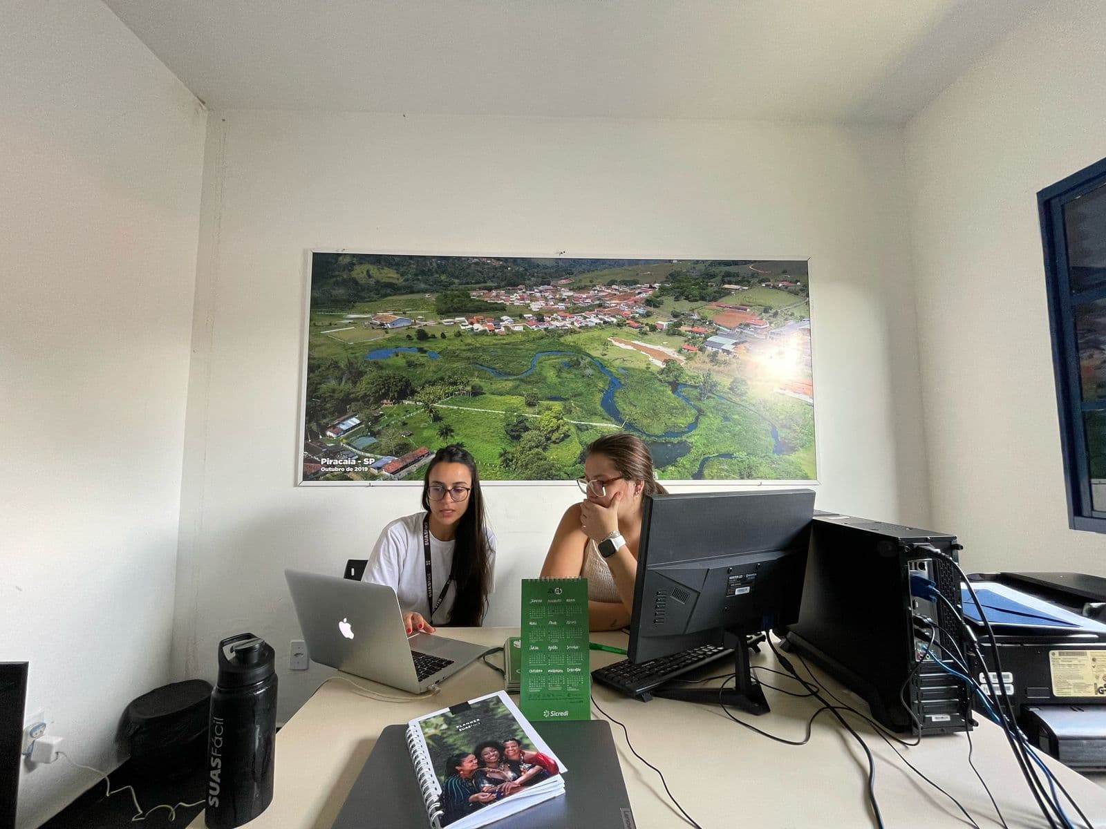 Duas profissionais em uma mesa de atendimento, com a plataforma aberta no computador